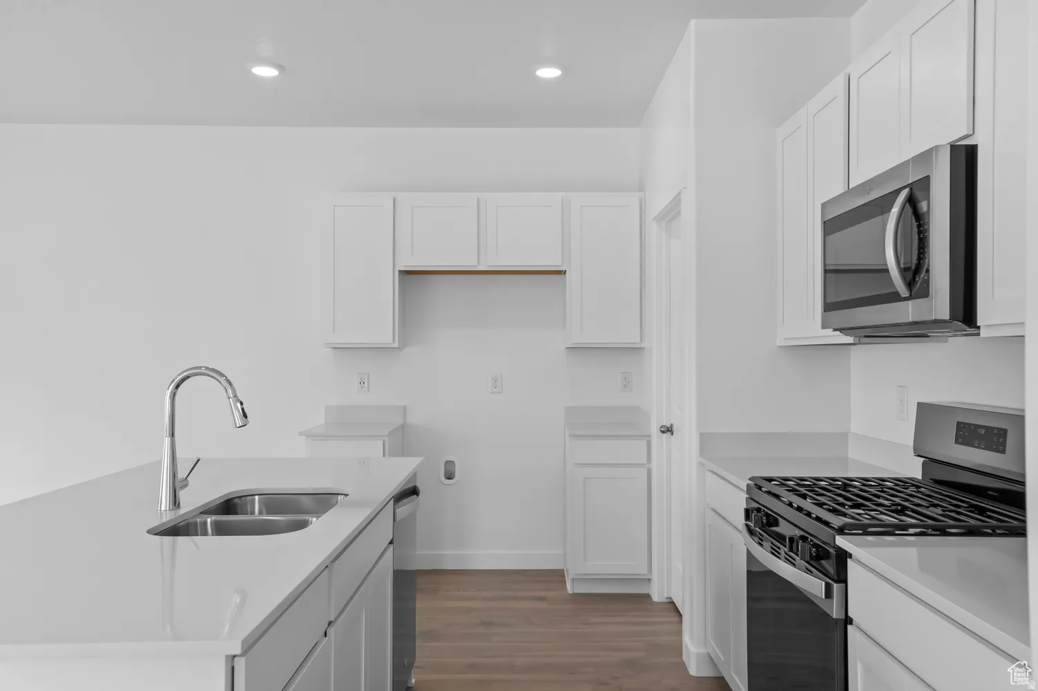 Modern kitchen featuring white cabinetry, light-toned countertops, a stainless steel microwave, a gas range, and a double basin sink with a pull-down faucet