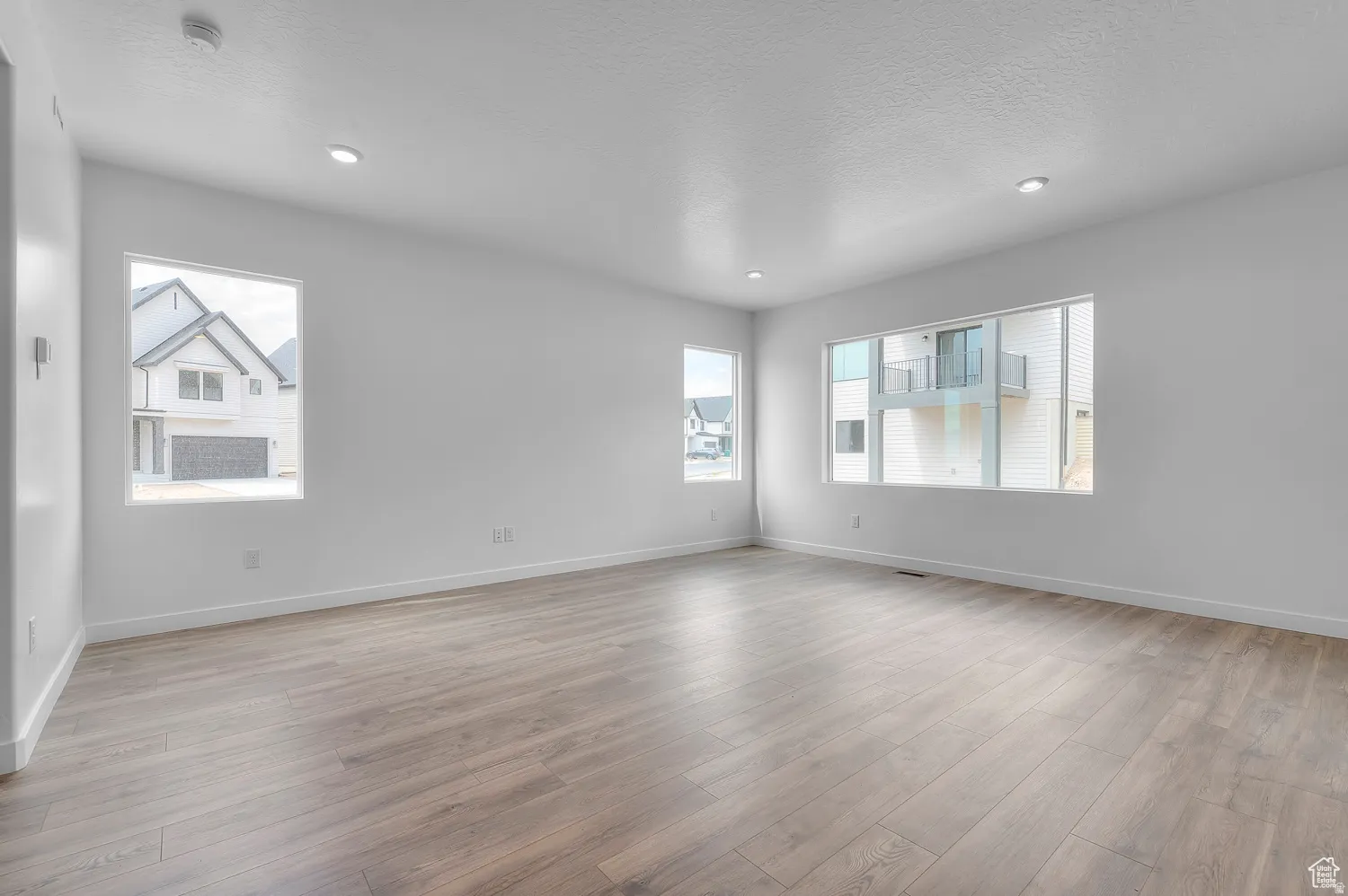 Spacious room featuring wood-finish flooring, white baseboards, and recessed lighting
