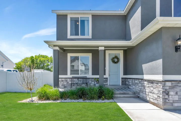 Contemporary stucco exterior with a stone veneer foundation, covered entryway, light blue front door, and a manicured lawn