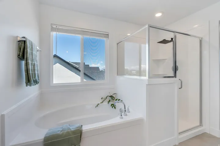 Bathroom featuring a built-in soaking tub, separate glass-enclosed shower with rain showerhead, recessed lighting, and a window with blinds
