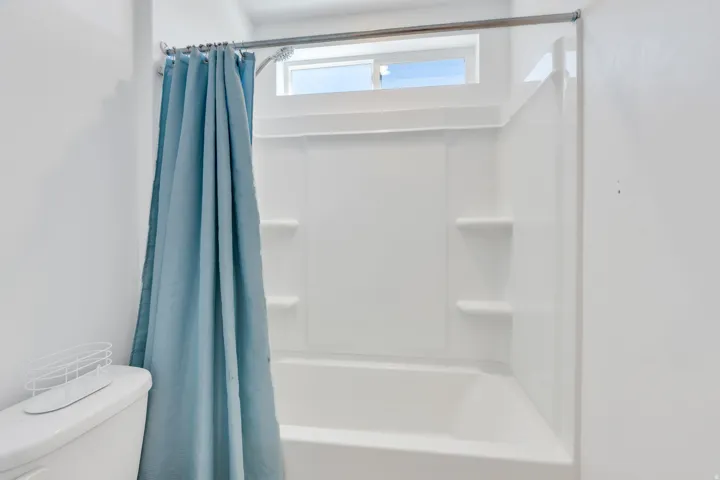 Bathtub and shower combination featuring a white surround with built-in shelving, a chrome shower rod, and an overhead window