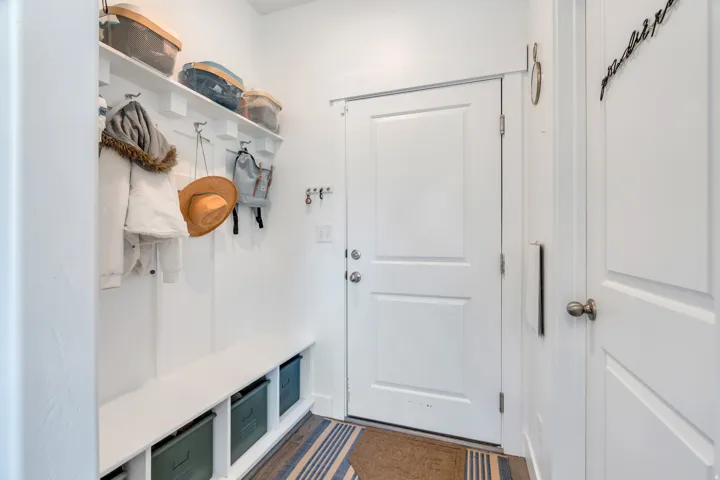 Mudroom entry featuring white shaker-style doors, built-in bench seating, integrated storage cubbies, and overhead shelving with wall-mounted hooks
