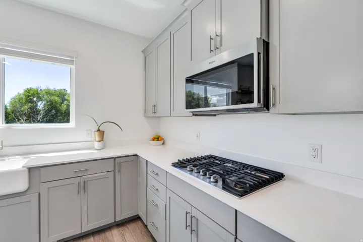 Modern kitchen featuring light gray cabinetry, white countertops, a stainless steel over-the-range microwave, a built-in gas cooktop, and a farmhouse sink