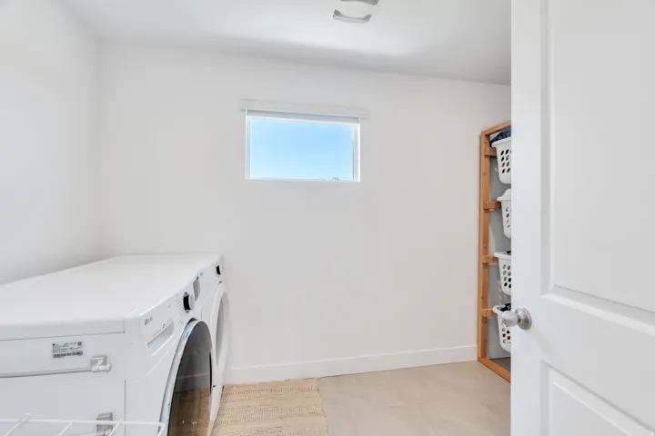Dedicated laundry area featuring a front-loading washer and dryer, light-toned flooring, and a window providing natural illumination