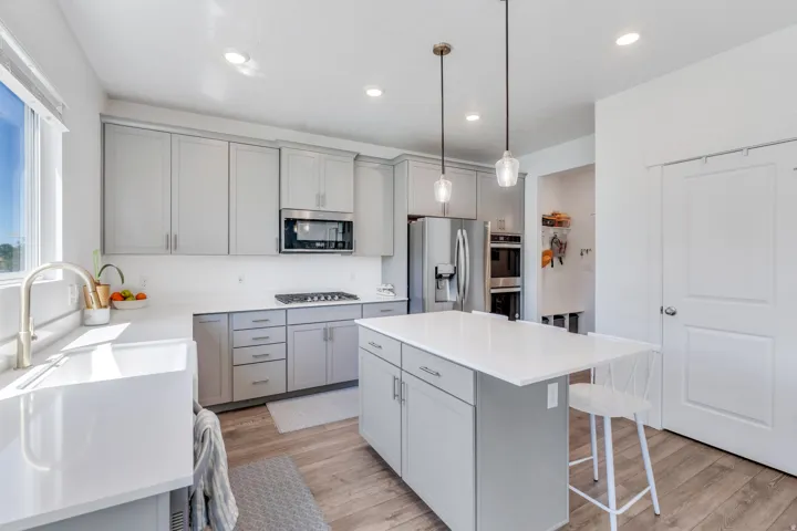 Modern kitchen featuring light gray cabinetry, an island with seating, a farmhouse sink, stainless steel appliances, and wood-finish flooring