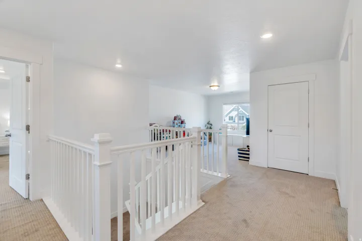 Upper-level landing featuring a white painted railing and neutral carpeting
