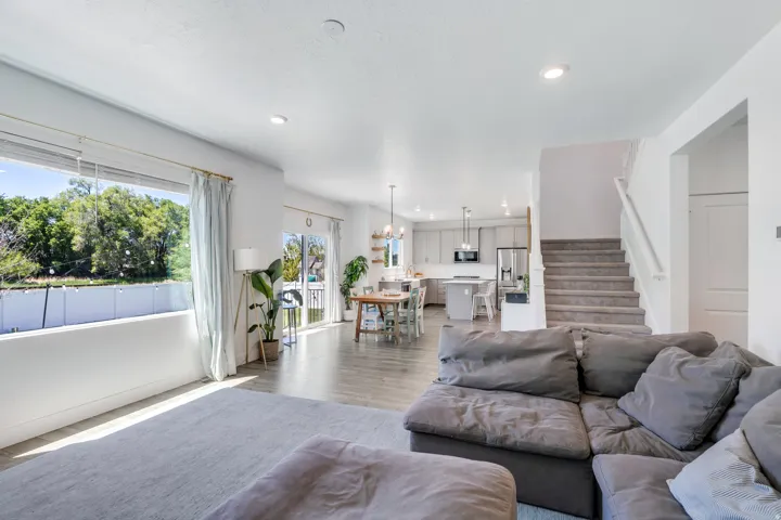 Open-concept living space featuring wood-finish flooring, a contemporary kitchen with light-toned cabinetry, a spacious window, and a carpeted staircase