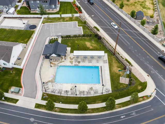 Outdoor swimming pool with an adjacent covered lounge area, multiple chaise lounges, and surrounding paved decking