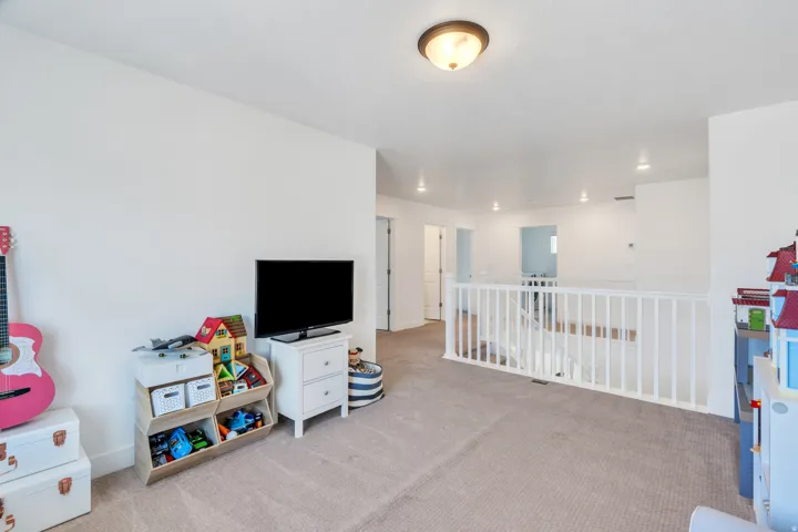 Spacious upper-level landing featuring neutral carpeting, white wall finishes, and a white balustrade overlooking the level below