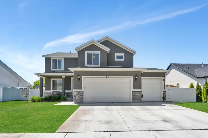Two-story stucco residence featuring a covered front porch with columns, a two-car garage, an additional single-car garage, and stone veneer accents