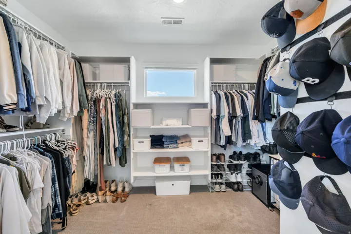 Carpeted walk-in closet featuring extensive built-in shelving, multiple hanging rods, and a high horizontal window providing natural light