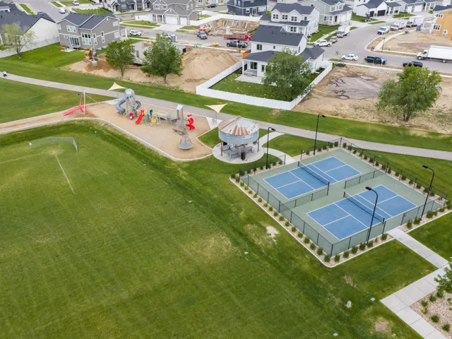 Expansive green field featuring a playground, two pickleball courts, a gazebo, and walking paths