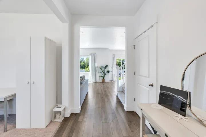 Bright interior hallway featuring wood-finish flooring, white walls, and a white paneled door