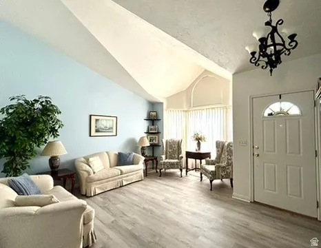 Spacious living area featuring vaulted ceilings, wood-finish flooring, a decorative chandelier, and an arched transom window above the entry door