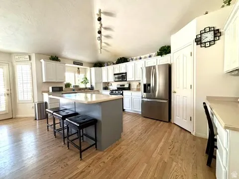 Bright kitchen featuring a central island, wood-finish flooring, white cabinetry, stainless steel appliances, and a window with natural light