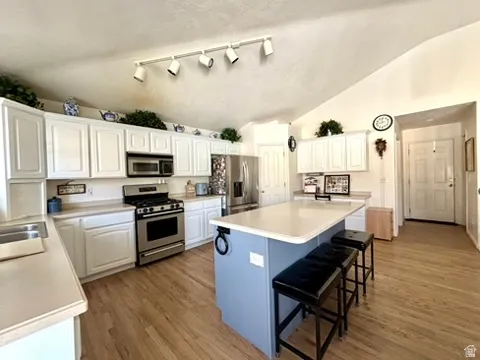 Kitchen featuring vaulted ceilings, wood-finish flooring, white cabinetry, a stainless steel range with an overhead microwave, and a central island with countertop seating