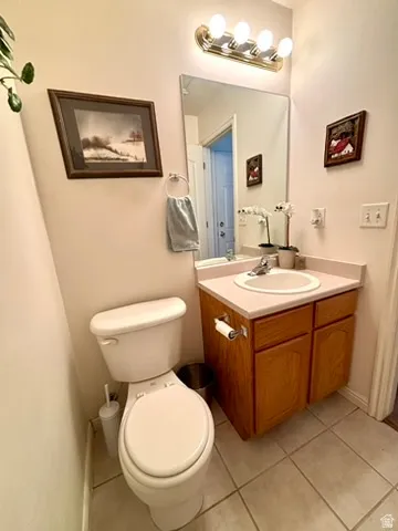 Bathroom featuring a white toilet, light-toned tiled flooring, and a vanity with wood-finish cabinetry