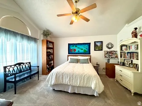 Carpeted interior space featuring a vaulted ceiling with an arched window, a ceiling fan with light fixture, and a built-in bookshelf