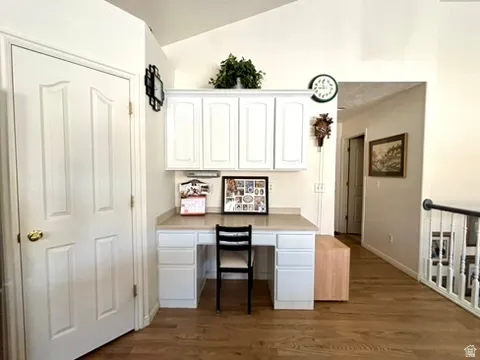 Built-in desk area featuring white cabinetry, light-toned countertop, and wood-finish flooring