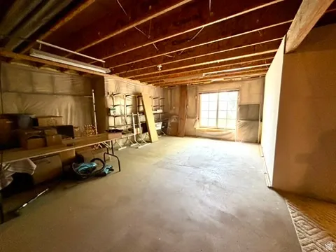 Unfinished basement space featuring exposed wood joists, concrete flooring, and a large window