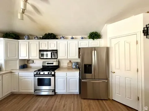 Kitchen featuring white cabinetry, wood-finish flooring, stainless steel appliances, and a vaulted ceiling with track lighting