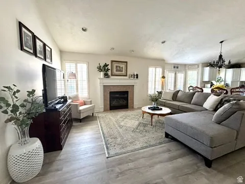 Spacious living area featuring light wood-finish flooring, recessed lighting, and a prominent fireplace with a stone surround and a white mantel