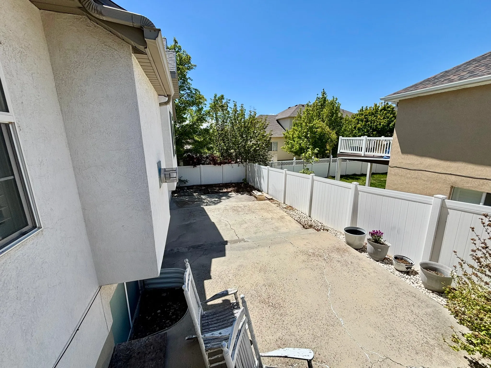 Paved outdoor area with a white privacy fence, stucco exterior, and window well
