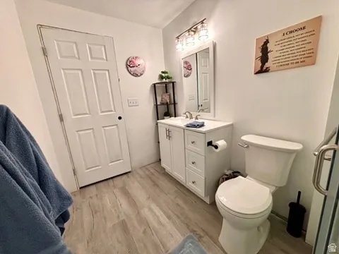 Bathroom featuring a white vanity with brushed nickel hardware, a white toilet, and wood-finish flooring