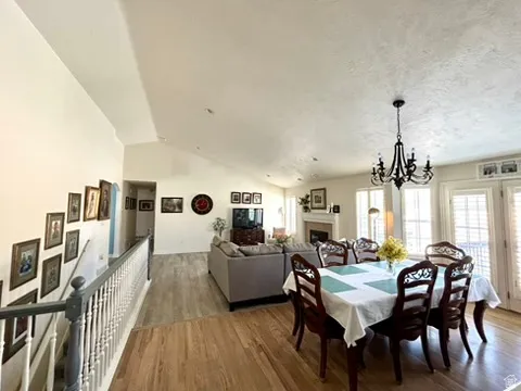 Open concept living and dining areas featuring wood-finish flooring, a vaulted ceiling, and an ornate chandelier