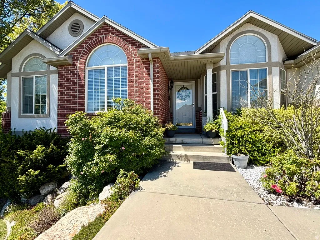 Brick and stucco exterior featuring arched windows, a covered entry, and a concrete pathway