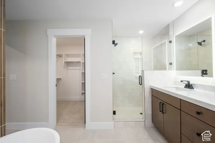 Bathroom featuring a walk-in shower with glass enclosure, single vanity with wood-finish cabinetry, illuminated mirror, and light-toned tile flooring