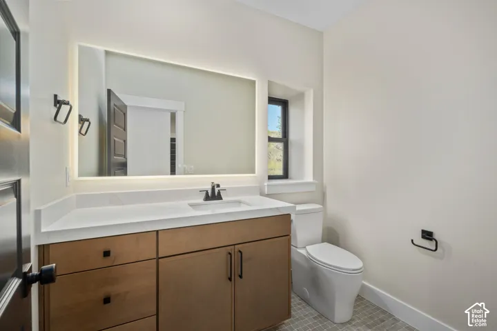 Bathroom featuring a wood-finish vanity with a white countertop, an integrated sink, a backlit mirror, and a window