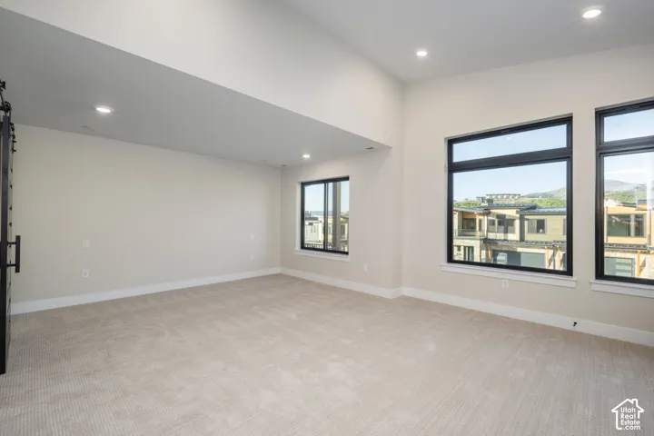 Spacious interior room featuring light-toned carpeting, recessed lighting, and expansive windows