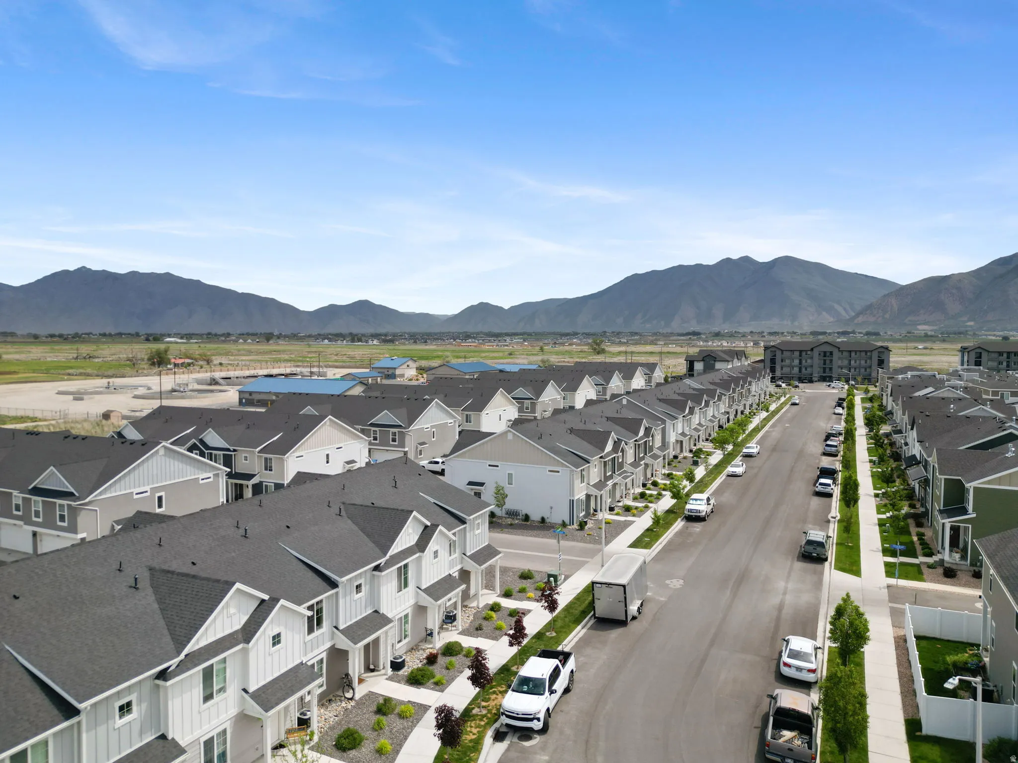 Aerial perspective showcasing a developed residential street lined with townhomes and detached properties, all featuring dark shingle roofs and light-colored siding