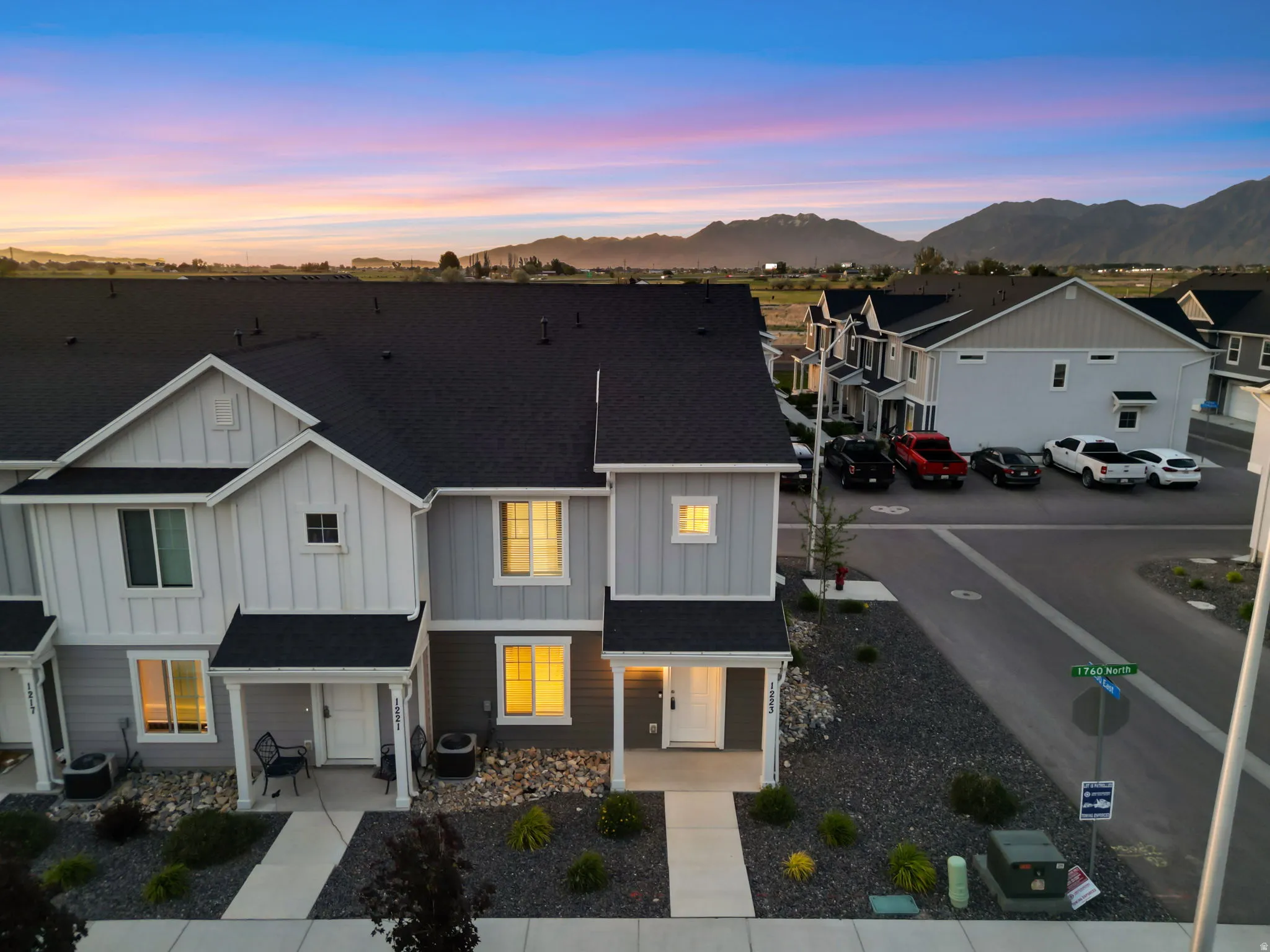 Modern townhome exterior featuring light gray and white siding, a dark shingle roof, and a welcoming covered porch entry