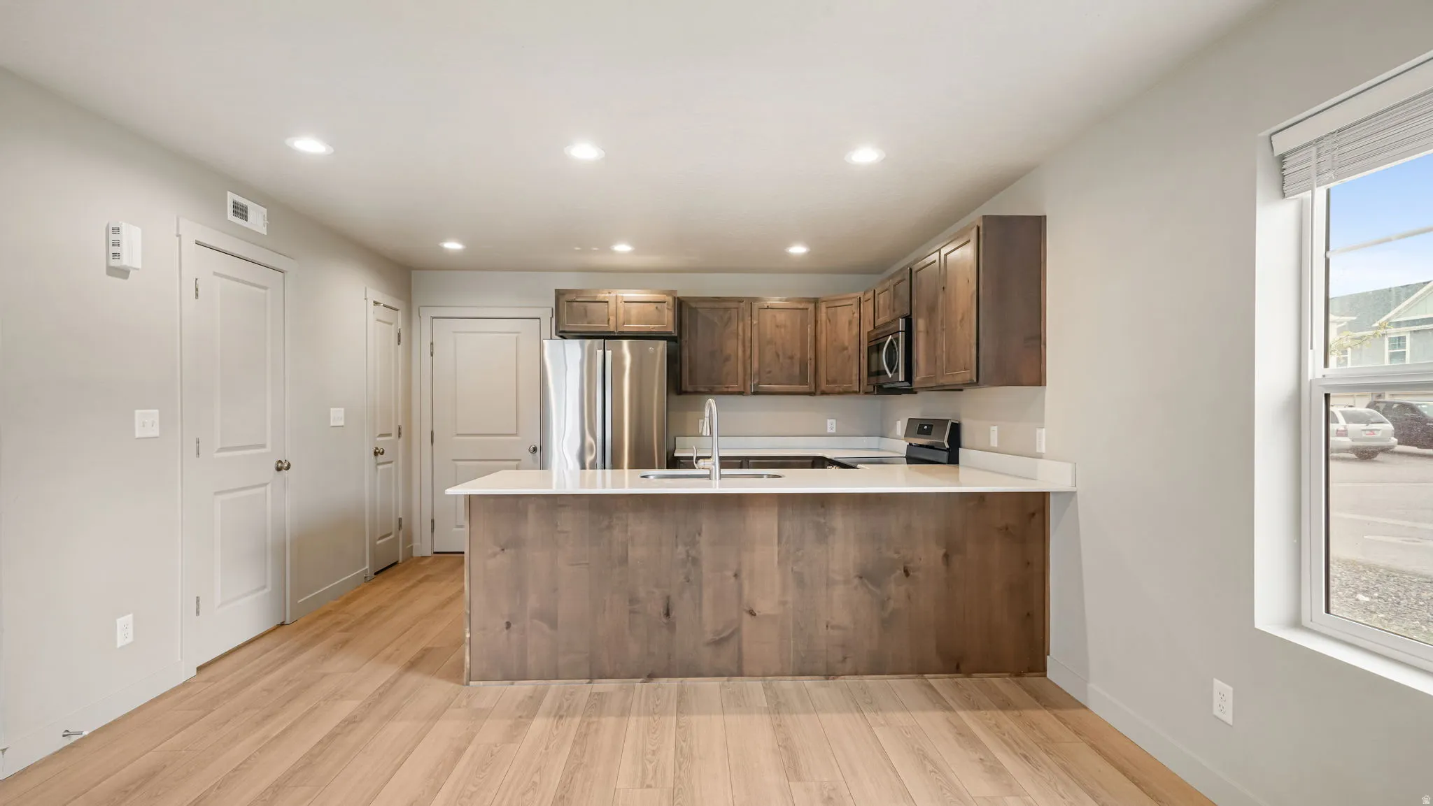 Open-concept kitchen with wood-finish flooring, stainless steel appliances, a breakfast bar island, recessed lighting, and white countertops