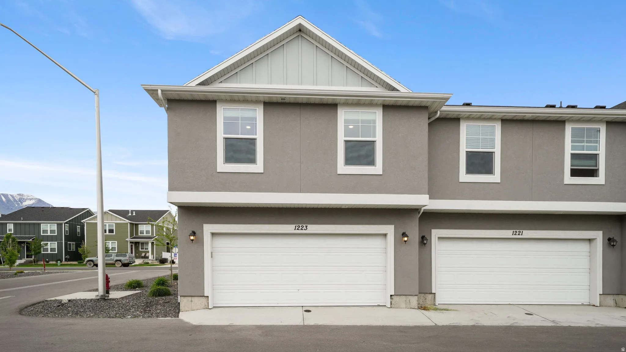 Contemporary townhouse exterior featuring a two-car garage, stucco siding, white trim, and a prominent gable roof