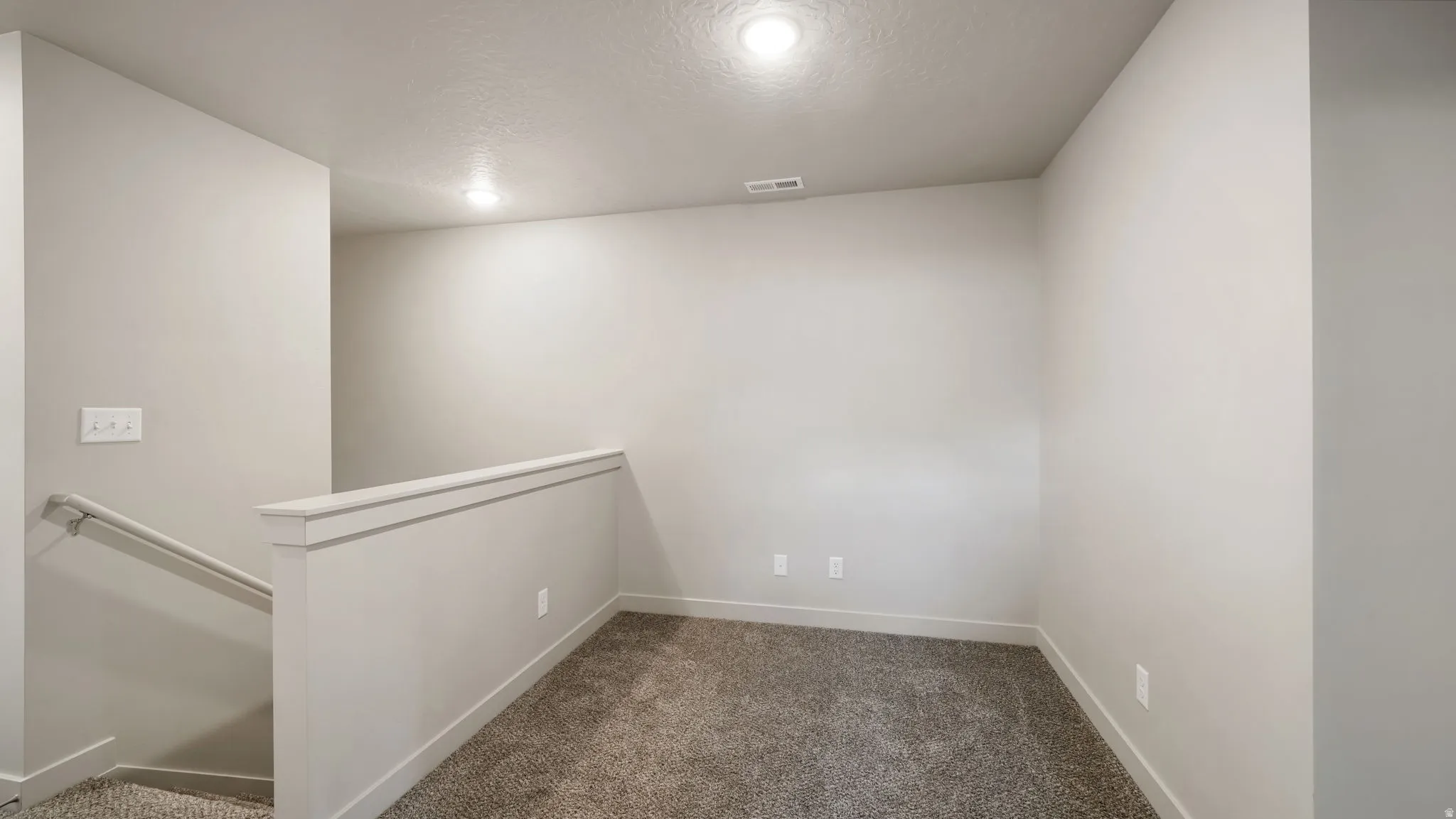 Carpeted loft area featuring a low wall with white trim, a visible stairway with handrail, recessed lighting, and neutral wall paint