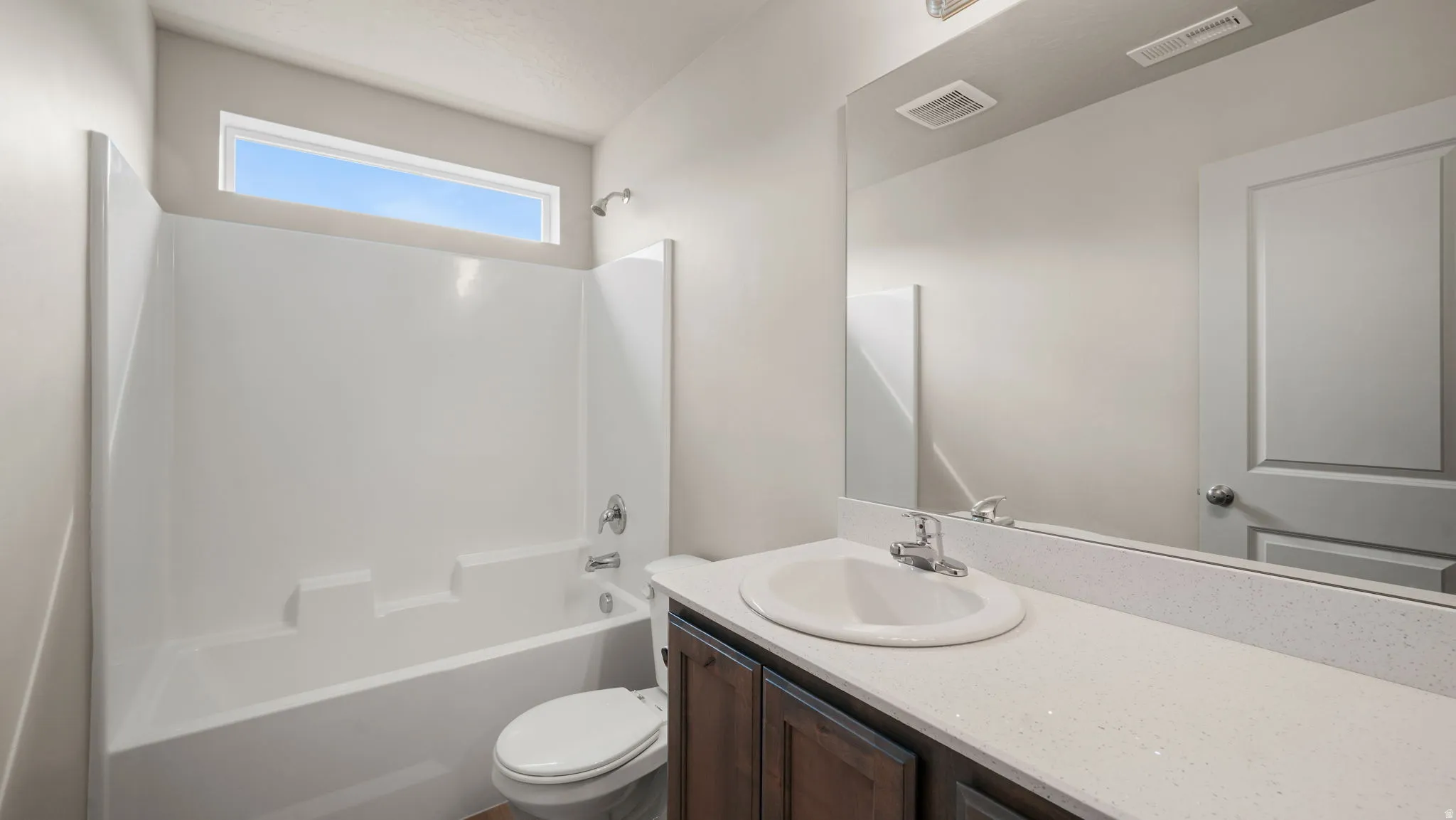 Full bathroom featuring a white tub/shower combination with a transom window, a dark wood-finish vanity, light-toned countertop, and an integrated sink with a chrome faucet