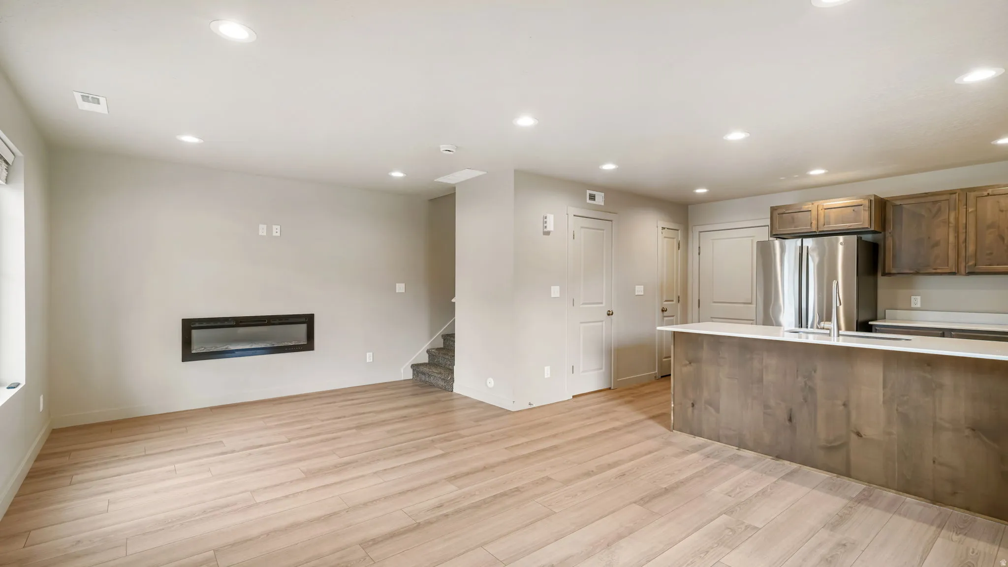 Open-concept living space featuring wood-finish flooring, recessed lighting, and a built-in electric fireplace