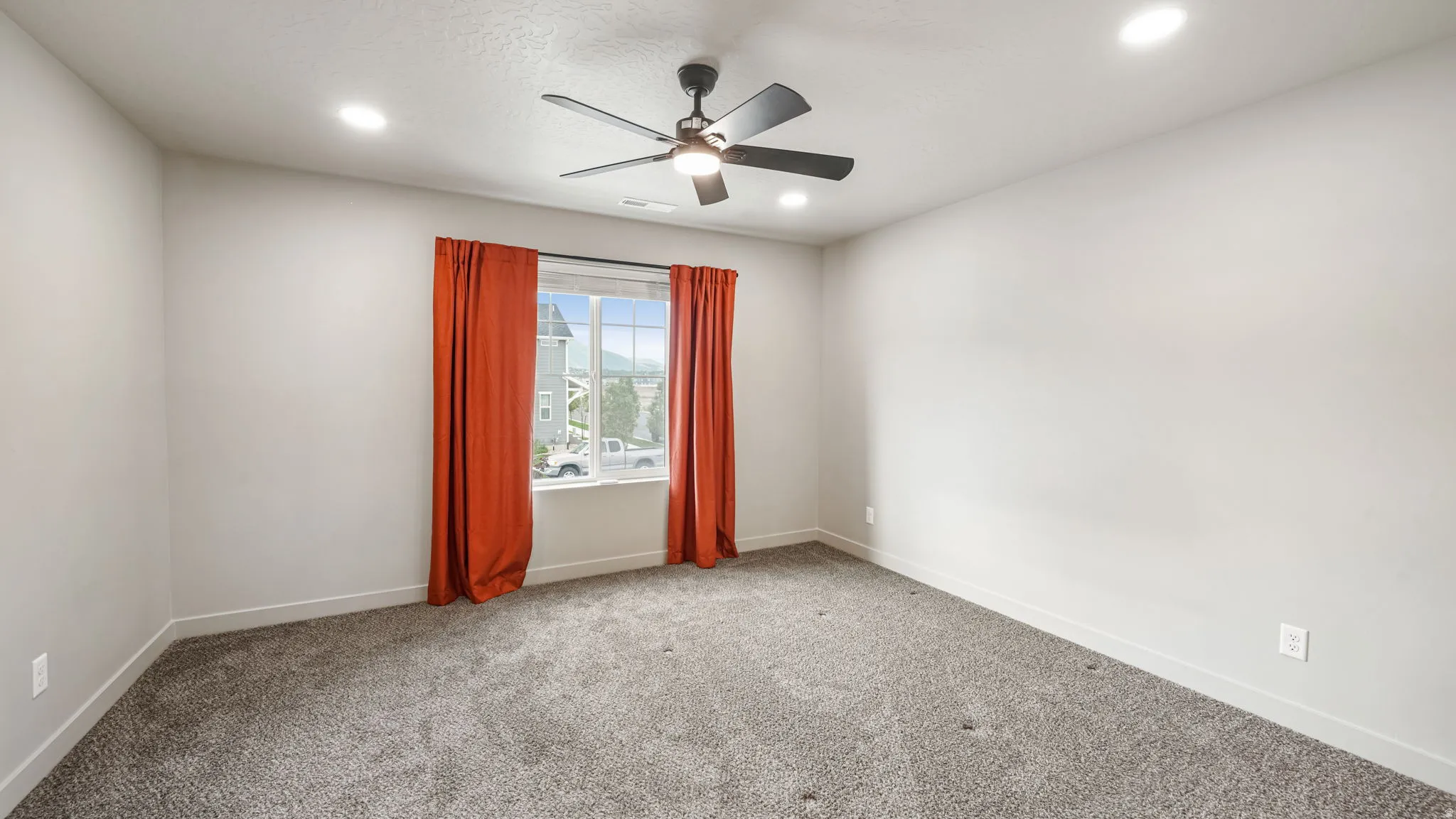 Spacious room featuring neutral carpeting, a multi-pane window, and a ceiling fan with integrated lighting