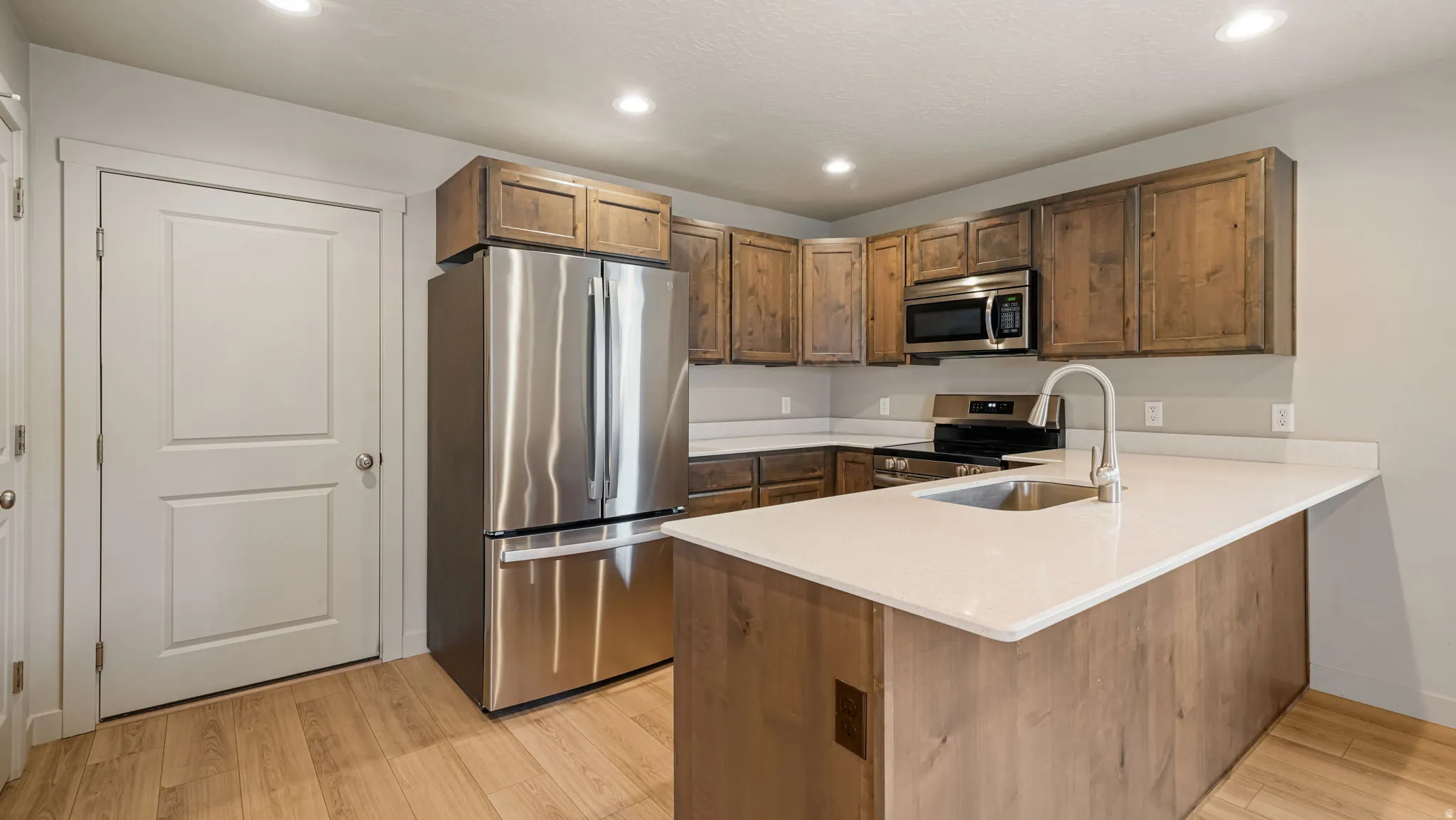 Kitchen featuring wood-finish flooring, white countertops, dark wood-tone cabinetry, and stainless steel appliances including a refrigerator, microwave, and range