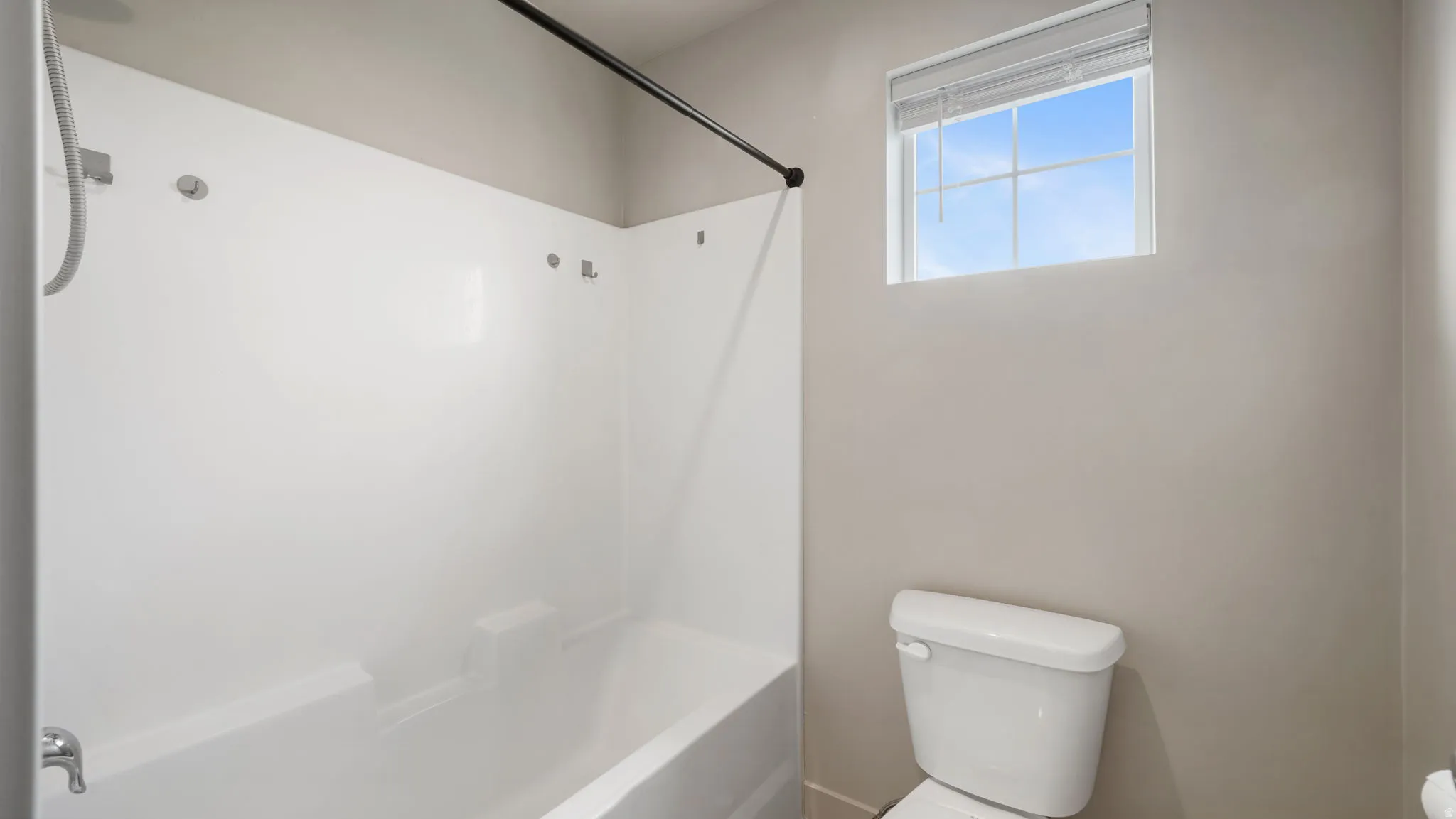 Bathroom featuring a white bathtub/shower combination with an integrated shelving unit, a white toilet, and a window with blinds