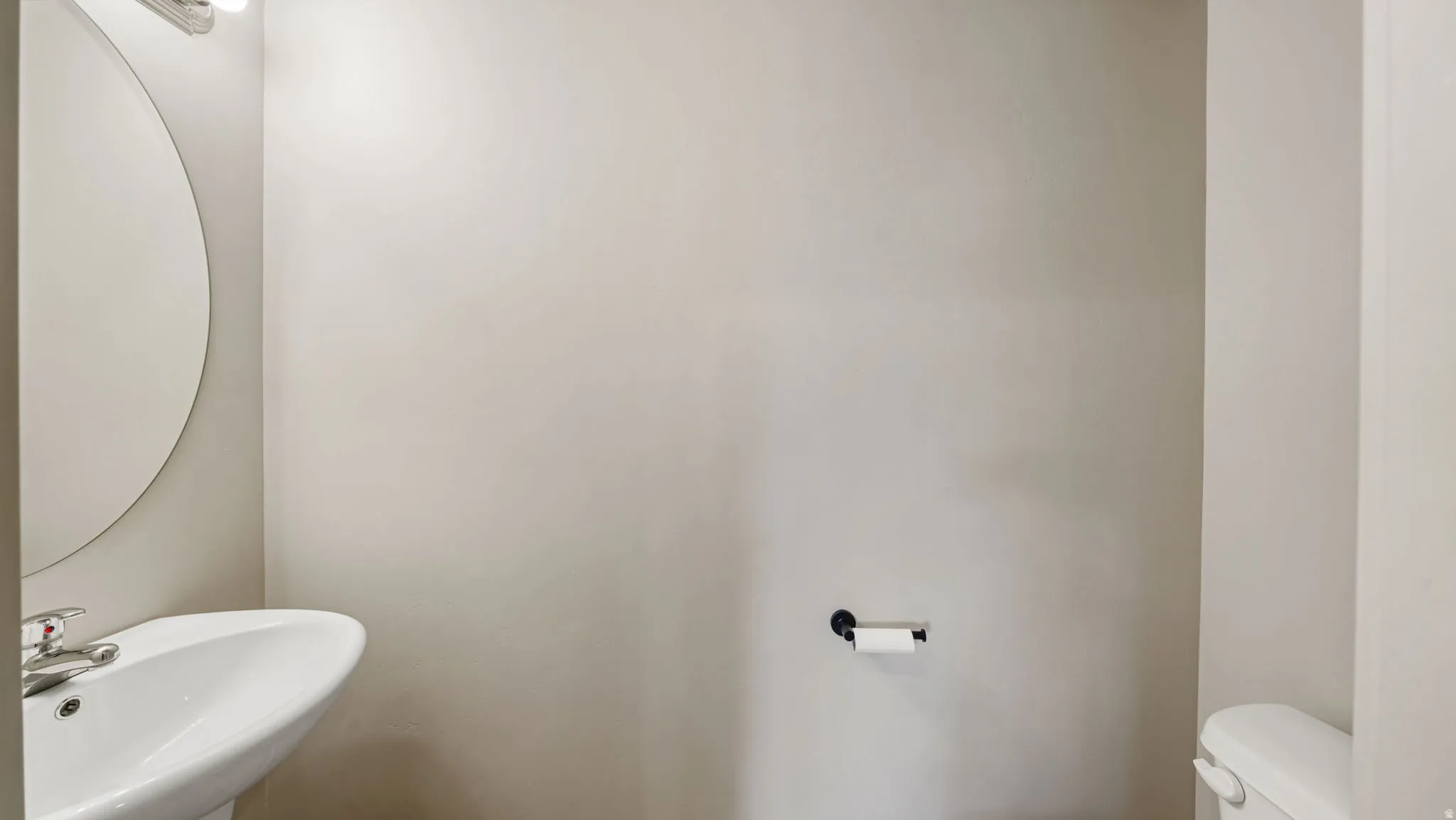 Pedestal sink with chrome faucet, circular wall mirror, and overhead vanity lighting