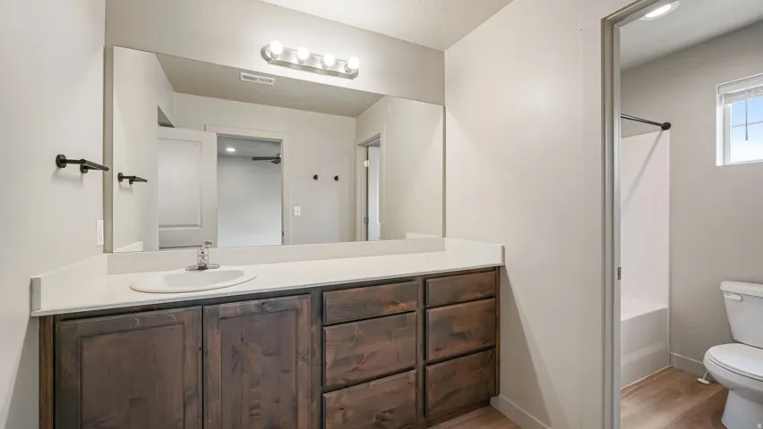 Bathroom featuring a long vanity with a light-colored countertop and integrated sink, rich wood-finish cabinetry, a large wall-mounted mirror, and a contemporary four-bulb light fixture