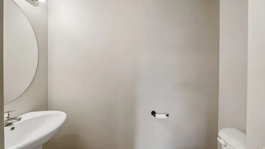 Pedestal sink with chrome faucet, circular wall mirror, and overhead vanity lighting
