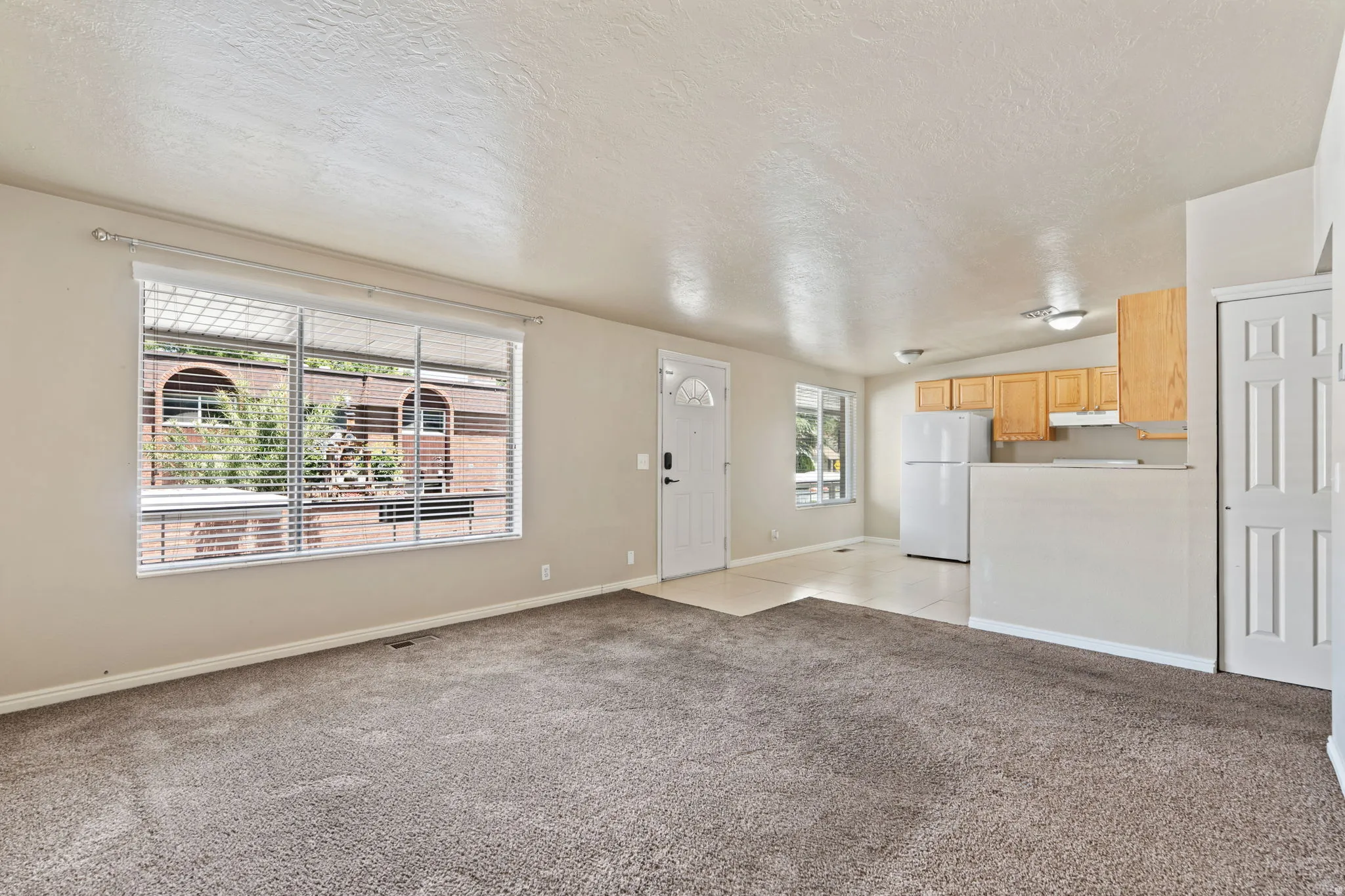 Open-concept living space featuring neutral-toned carpeting, a large window with blinds, and white trim