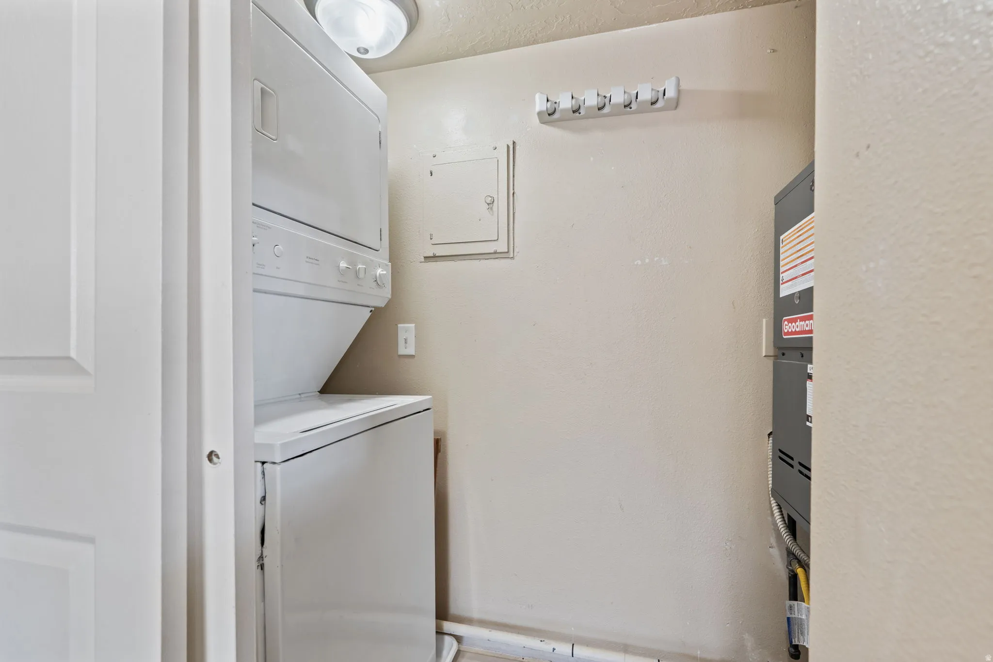 Dedicated laundry area featuring a stacked washer and dryer, ceiling-mounted light fixture, and wall-mounted utility hooks