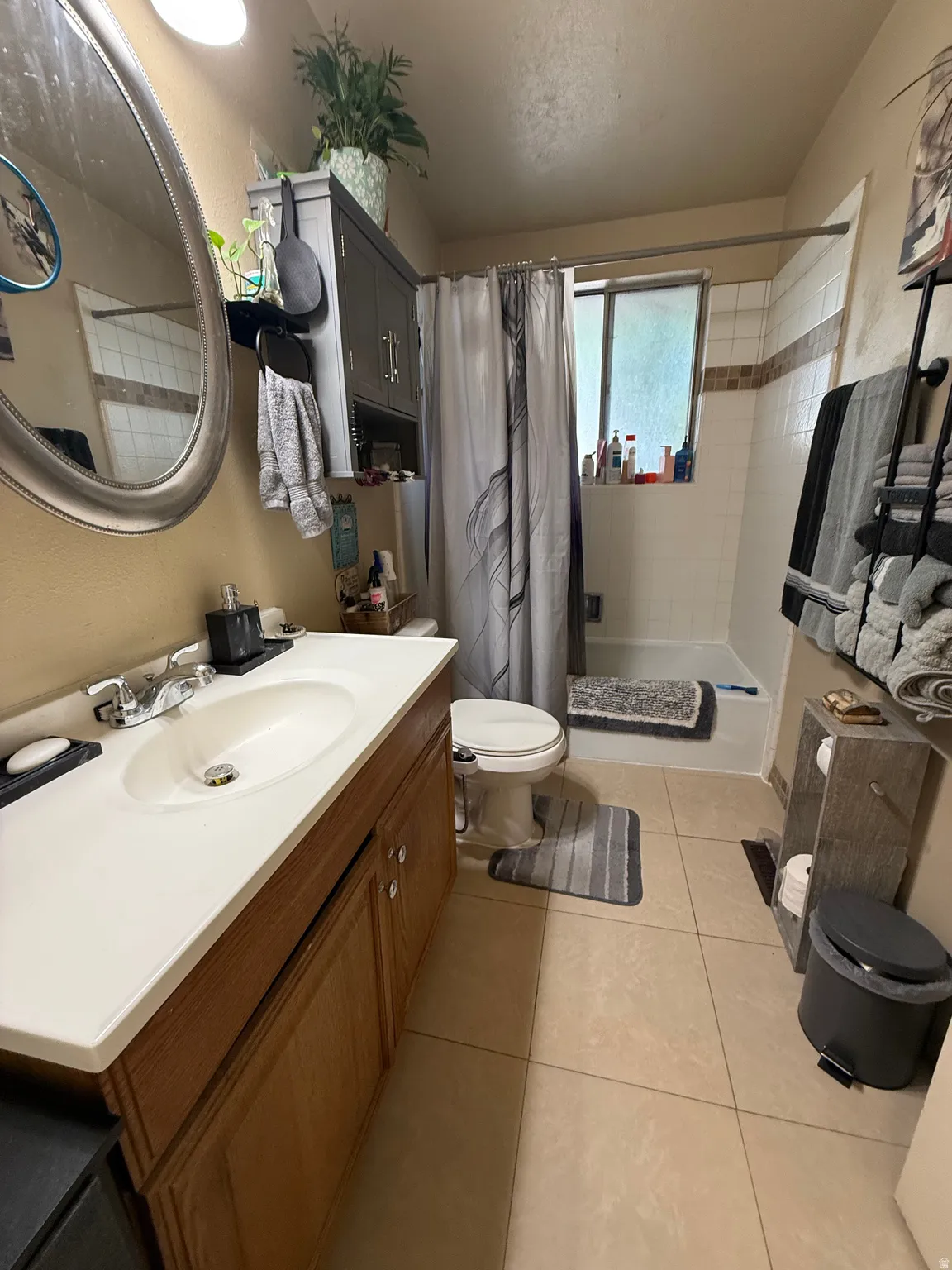 Bathroom featuring a vanity with an integrated sink, a built-in over-toilet cabinet, and a shower-tub combination with a window