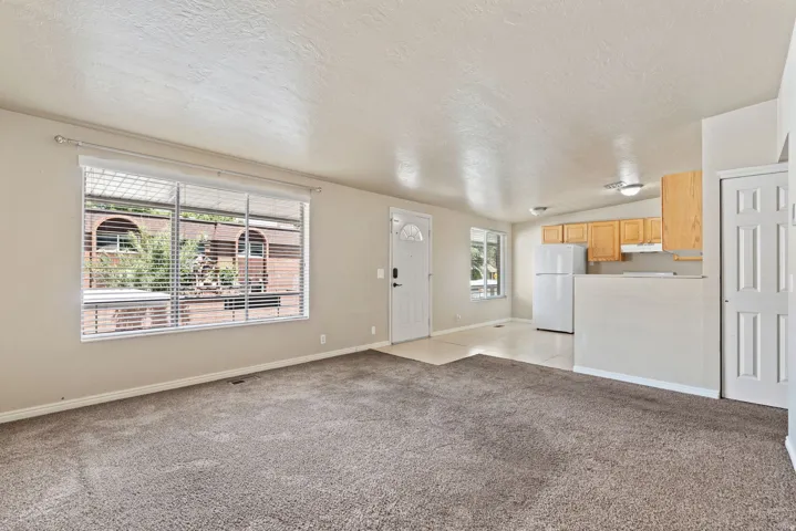 Open-concept living space featuring neutral-toned carpeting, a large window with blinds, and white trim
